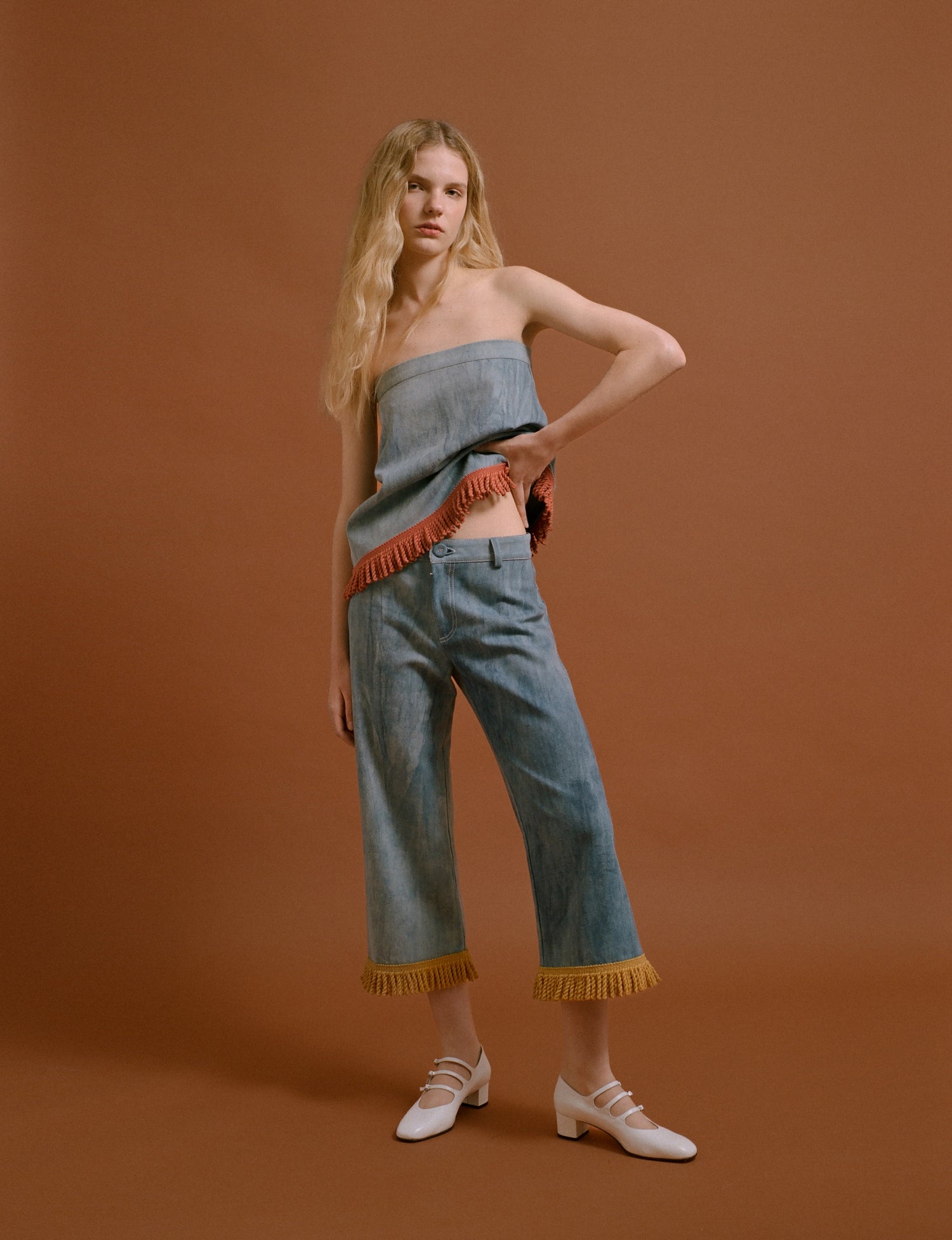 Blonde woman posing with a denim top, yellow embroidered denim pants and white shoes.