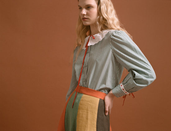 Blonde woman wearing a long-sleeved blue striped button-down shirt and a high-waisted skirt