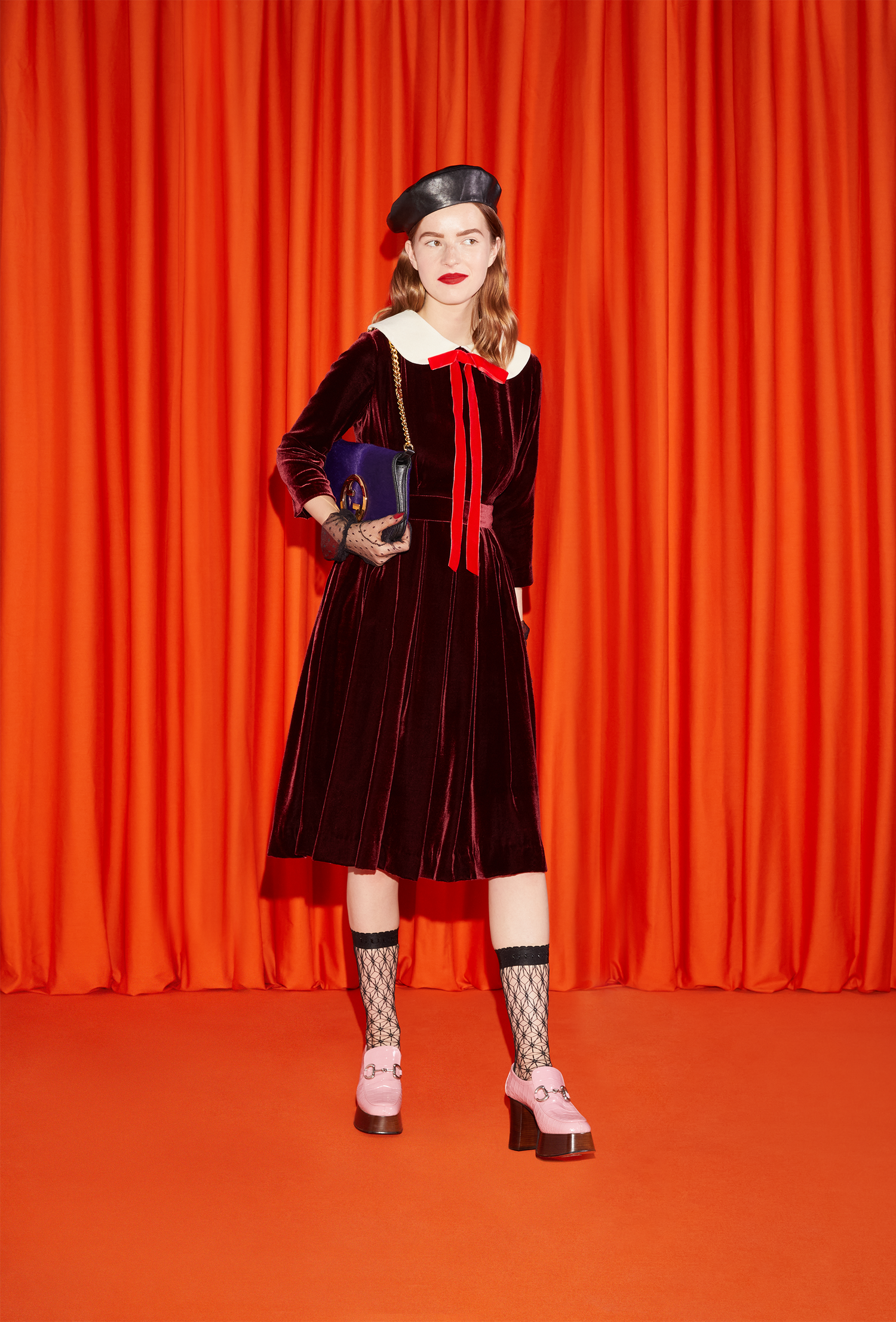Model wearing a burgundy velvet dress, mesh stockings and matching white shoes.