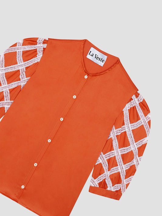 Shirt made of orange colored silk and rounded collar. It has sleeves above the elbow with raw lace detail. Button closure.