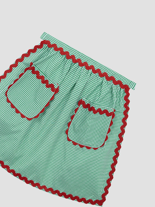 Green vichy quilted apron with red piping detail and two matching pockets on the front.