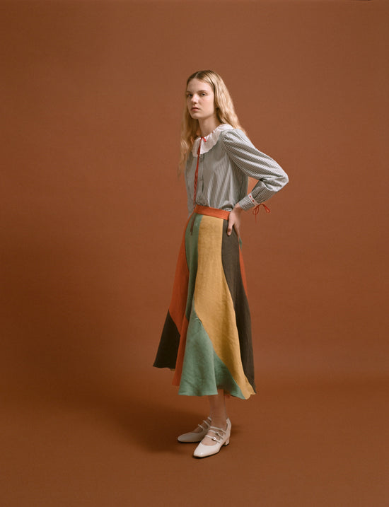 Model with long-sleeved blue striped shirt and long tricolor skirt