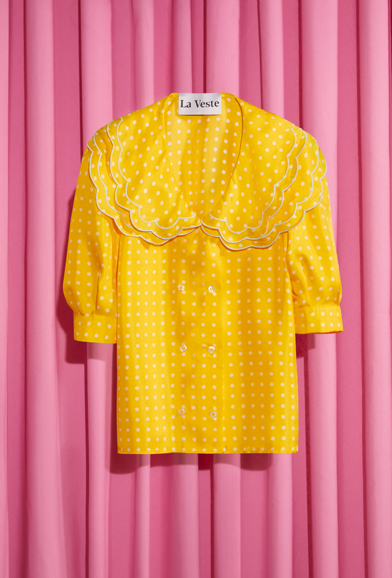 Yellow shirt with three-quarter sleeves, white dots and baby collar exposed on a fuscia background.