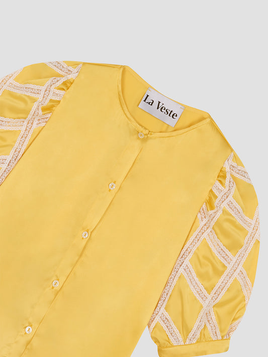 Shirt made of mustard colored silk and rounded collar. It has sleeves above the elbow with raw lace detail. Button closure.