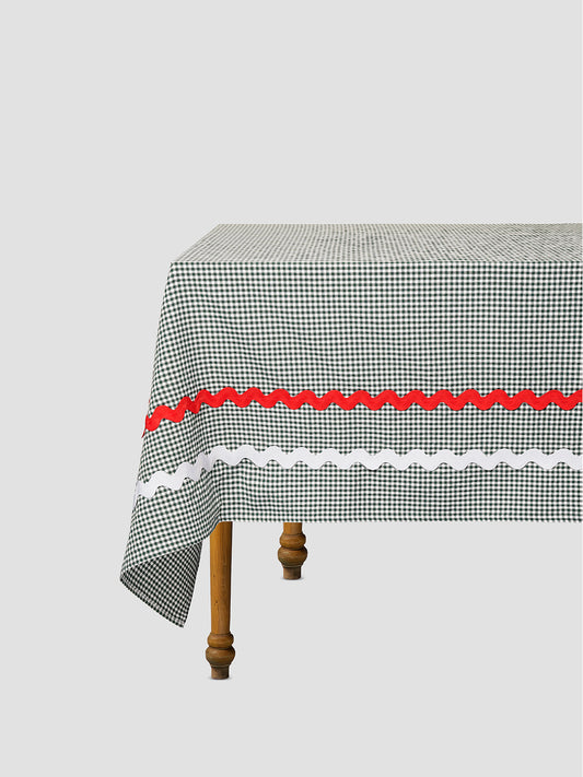 Green checkered tablecloth with white and red trim details placed on a table top
